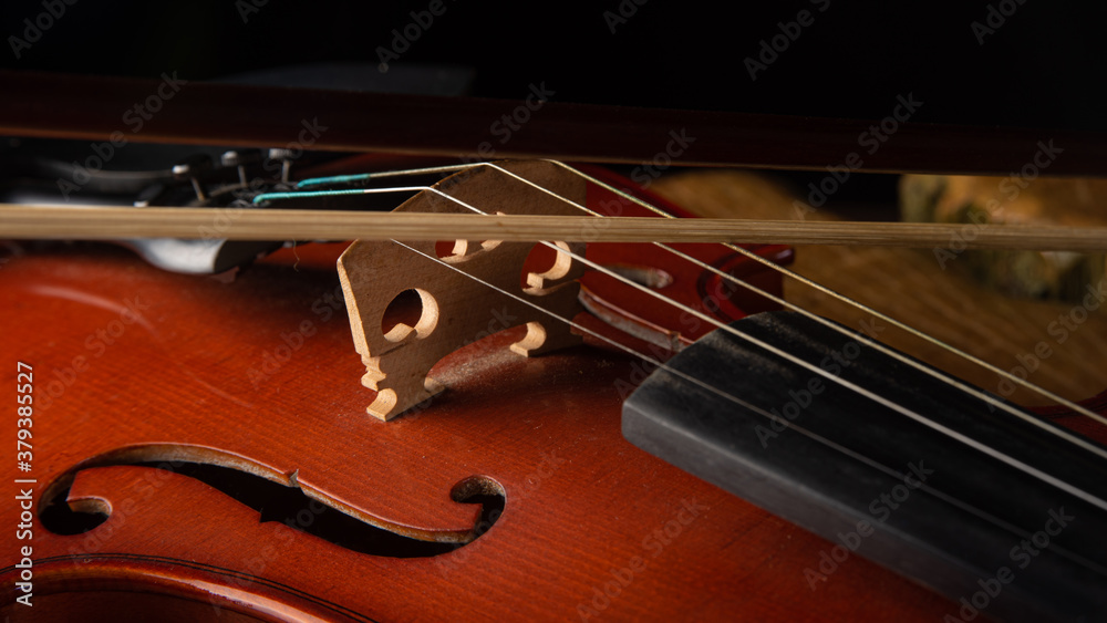 Details of an old and beautiful violin on a rustic wooden surface and black background, low key portrait, selective focus. Details of an old and beautiful violin on a rustic wooden surface and black background, low key portrait, selective focus.