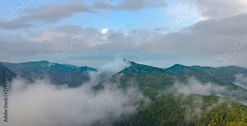 Fog in the mountains. Green and yellow forest on the mountain slopes. Wet fog in the valley. Sky with clouds. Takmak mountain in park Krasnoyarsk pillars. Natural blur.