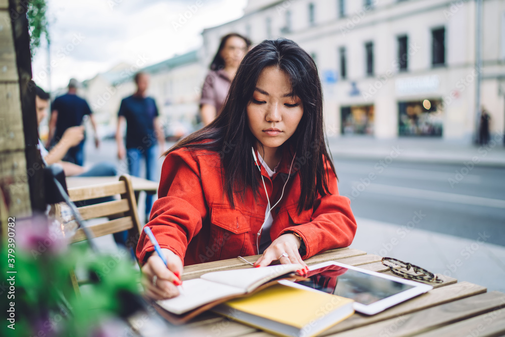 Serious female student taking notes in notebook in outdoor cafe
