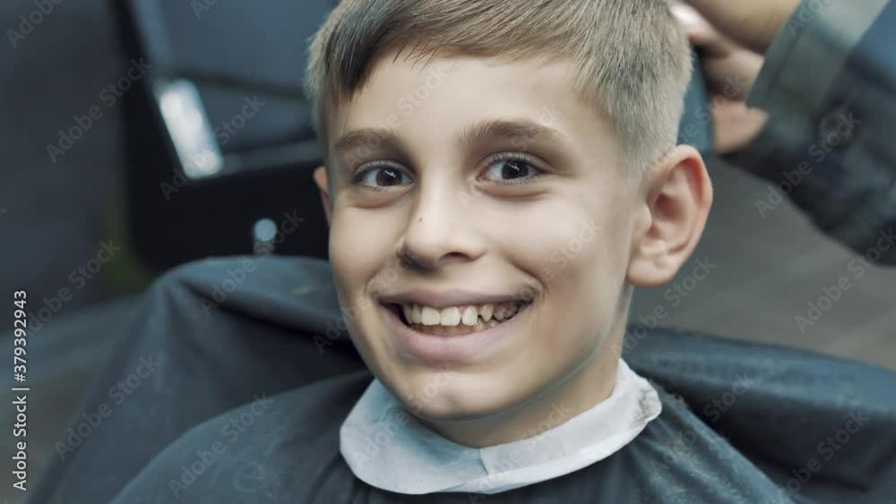 Close-up portrait of a cute handsome smiley caucasian boy sitting barbershop getting his head shaved vintage style haircut professional hairdresser hairstylist barber. healthcare lifestyle Close-up portrait of a cute handsome smiley caucasian boy sitting barbershop getting his head shaved vintage style haircut professional hairdresser hairstylist barber. healthcare lifestyle