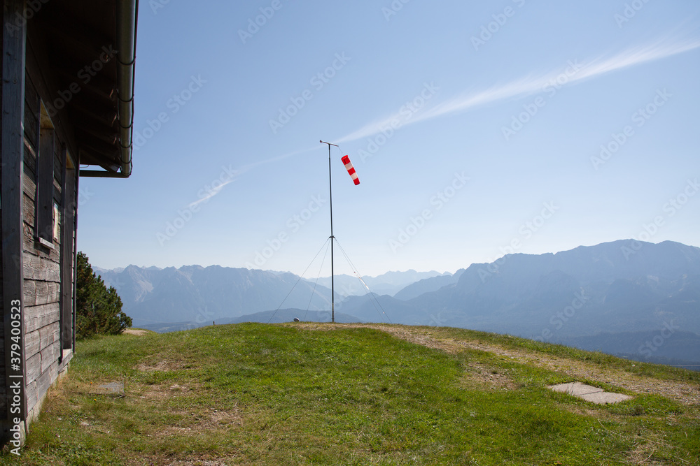 Launch site of paragliders with red and white windsocks and wooden hut. In the background mountain peaks in the German Alps Launch site of paragliders with red and white windsocks and wooden hut. In the background mountain peaks in the German Alps