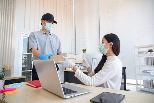Delivery man bring parcel to customer by wearing surgical mask and gloves in the office