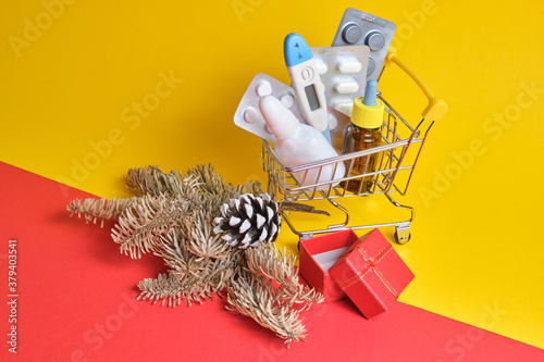 shopping cart with medicines on yellow-red background, buying medicines before christmas and new year, cold and flu season photo