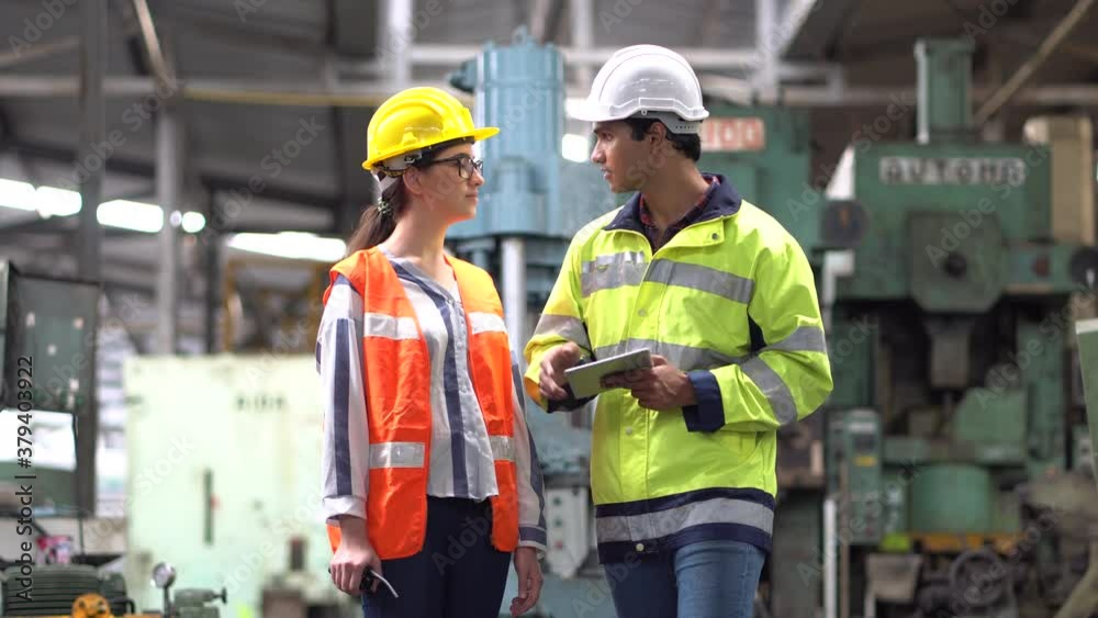 Indian Engineer in Hard Hats and Inspector woman talking and inspect machines with tablet computer in the Industrial factory. walking to camera and out of focus Indian Engineer in Hard Hats and Inspector woman talking and inspect machines with tablet computer in the Industrial factory. walking to camera and out of focus