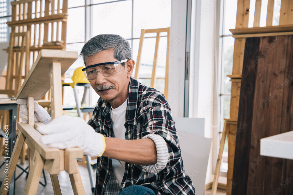 A senior carpenter holds wooden table elements interior accessories for further refinement within a building or condominium. Construction concept.
