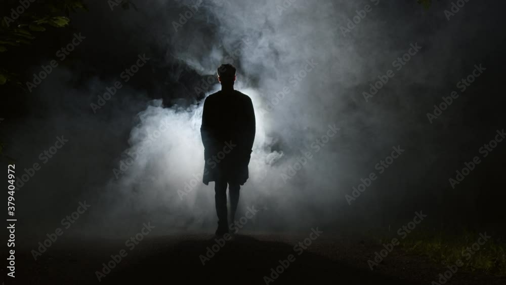 A silhouette of a man is walking through mist