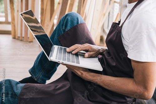A senior carpenter using laptop for searching wooden interior accessories for further refinement within a building or condominium. Construction concept.