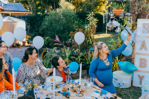 Female friends taking selfie with pregnant woman at a baby shower. Mobile photography, party decorations in white and blue colors, baby boy photo