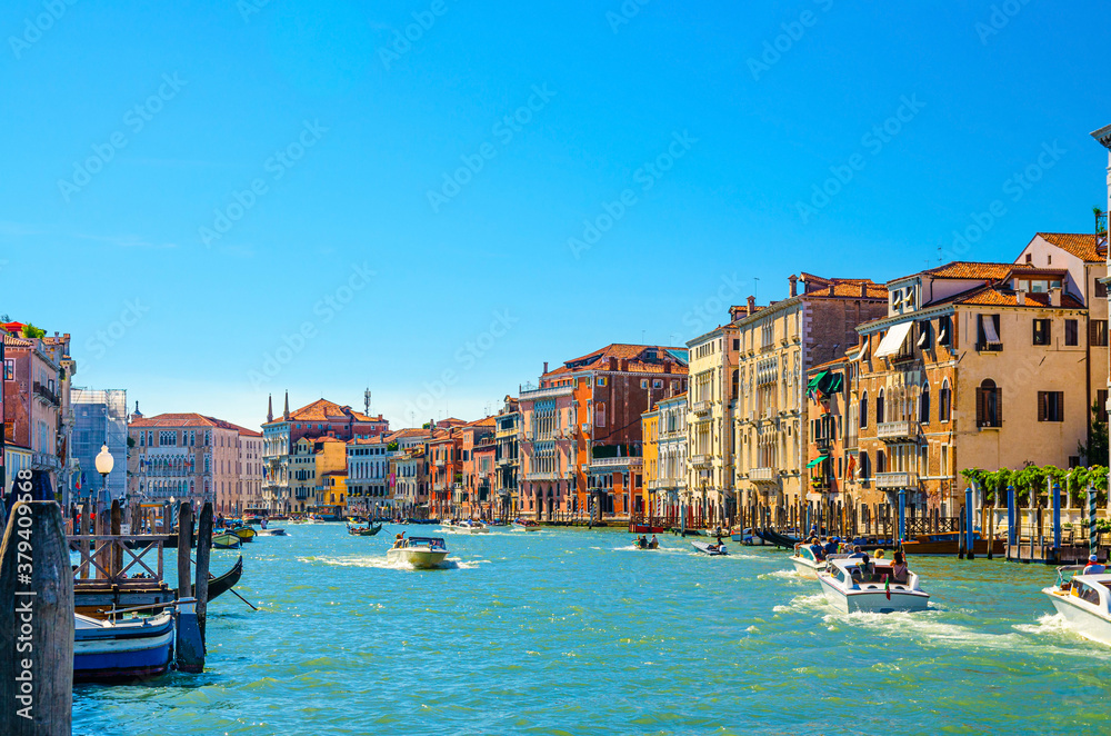 Venice cityscape with Grand Canal waterway, Venetian architecture colorful buildings, gondolas and yacht boats sailing Canal Grande, blue sky in sunny summer day. Veneto Region, Northern Italy.