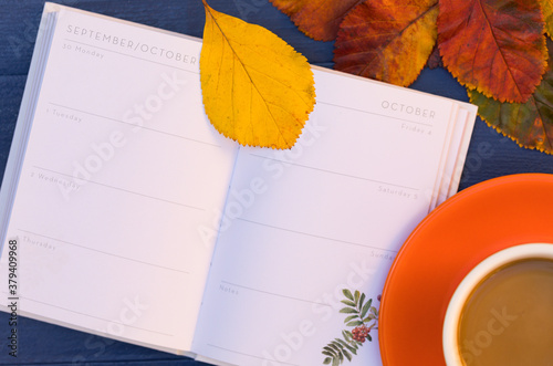 Desktop Autumn Composition with Bright Fallen Leaves, Open Empty Page of Diary for October and Orange Cup of Coffee - Background, Copy Space, Frame, Top View. Golden Leaf Fall Mood.