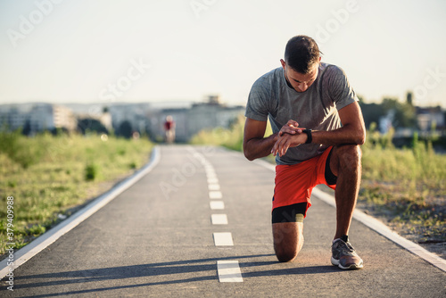 Young handsome sporty jogger taking break from exercising outdoors looking on a smart fitness watch photo