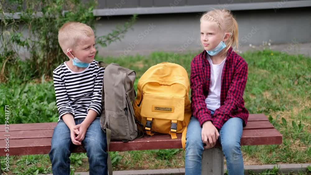 4k back to school. Girl and boy children sit talking on bench near the ...
