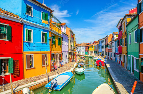 Colorful houses of Burano island. Multicolored buildings on fondamenta embankment of narrow water canal with fishing boats in sunny day, Venice Province, Veneto Region, Northern Italy. Burano postcard © Aliaksandr