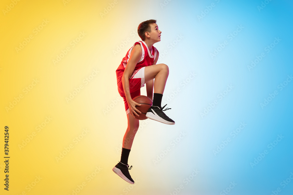 In fly. Full length portrait of young basketball player in uniform on gradient studio background. Teenager confident posing with ball. Concept of sport, movement, healthy lifestyle, ad, action, motion