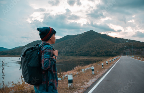 A man carrying a bag he stands on a mountain road and beautiful natural scenery. He looked forward to reaching the destination of that high mountain in Thailand. Goal successful concept