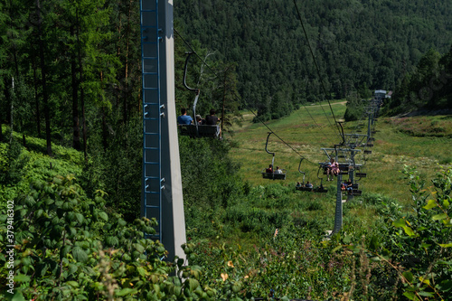 old cable car seats with people among trees in green forest on hill in mountains  sunny summer