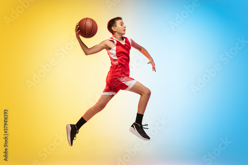Jump high. Full length portrait of young basketball player in uniform on gradient studio background. Teenager confident posing with ball. Concept of sport, movement, healthy lifestyle, ad, action