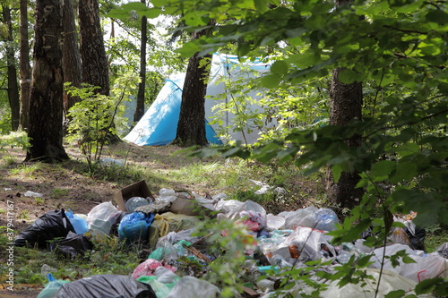 Obraz na płótnie Big garbage pile in the forest next to a camp tent among the green trees in Park on a Sunny summer day, plastic littering the wildlife with vacationers people w salonie