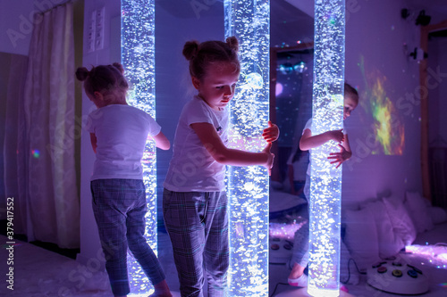 Child in therapy sensory stimulating room, snoezelen. Autistic child interacting with colored lights bubble tube lamp during therapy session. photo