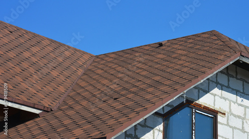 A close-up on a roofing construction of a brick house covered with asphalt shingles with roofing flashing installed in problem areas.