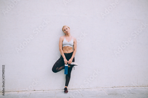 Sportswoman standing on one leg and leaning on wall