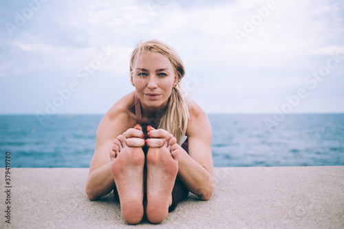 Portrait of good looking Caucasian woman practicing Paschimottanasana exercise enjoying morning time at coastling for care about mind and body, experienced professional yogi training at nature photo