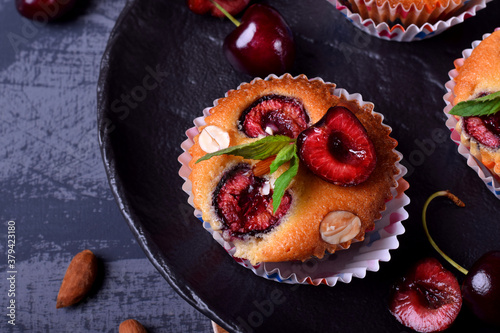 Muffins with cherry in paper cups topped with mint served on the black plate