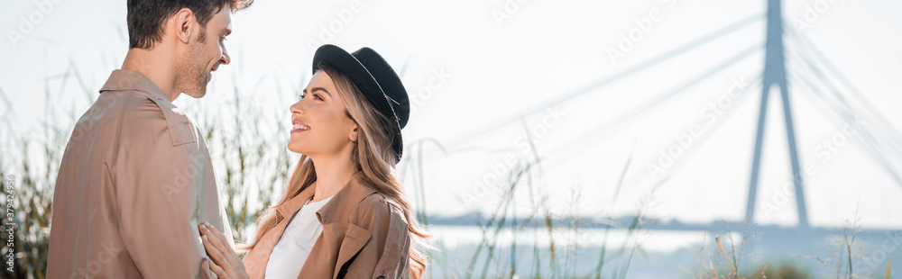 Naklejka premium panoramic shot of woman in hat and man looking at each other outside