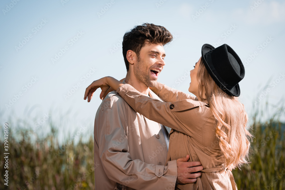 blonde woman in hat hugging excited man in trench coat