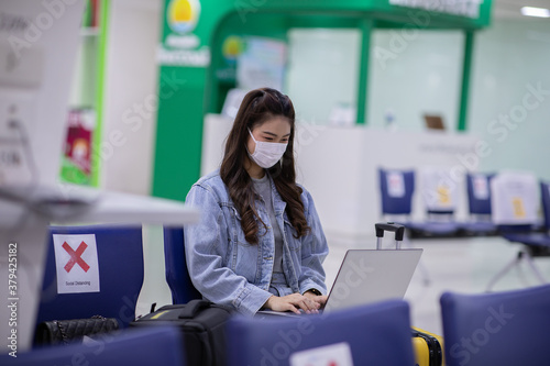 Asian young woman wearing face maks using laptop computer at airport Due Covid-19 flu virus pandemic and protection