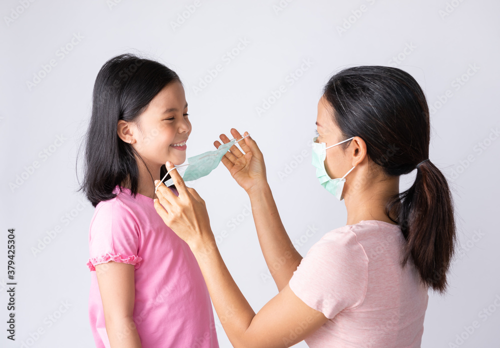 Asian mother in pink shirt wearing face mask to her daughter healthy on white to prevent protect PM2.5 dust, smog, air pollution, flu, coronavirus and COVID-19. Healthcare concept.