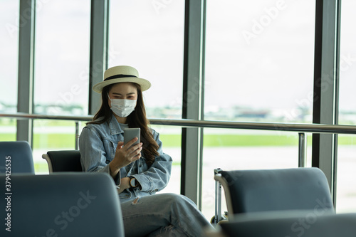 Asian young woman traveller wearing face maks using mobile phone at airport Due Covid-19 flu virus pandemic and protection © 220 Selfmade studio