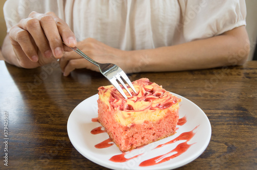 Female eating raspberries cheese cake on white plate.