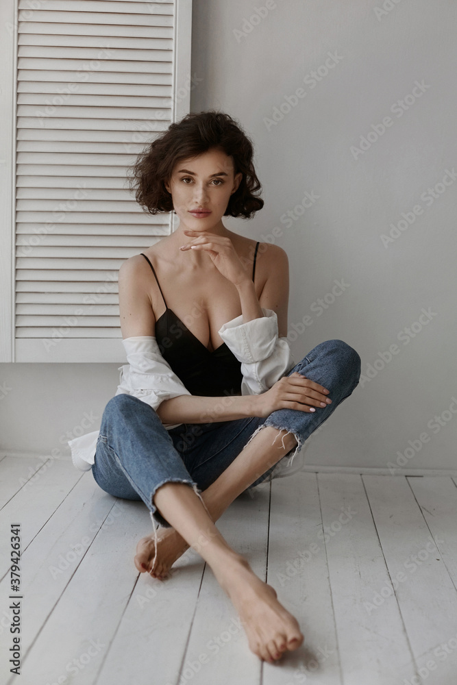 A gorgeous model girl with slim body wearing blue jeans and seductive top sits on the floor indoors A gorgeous model girl with slim body wearing blue jeans and seductive top sits on the floor indoors