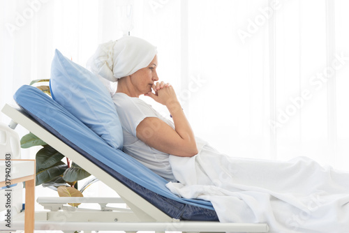 Side view of senior breast cancer patient wearing a headscarf laying in bed and praying in the hospital room, cancer concept