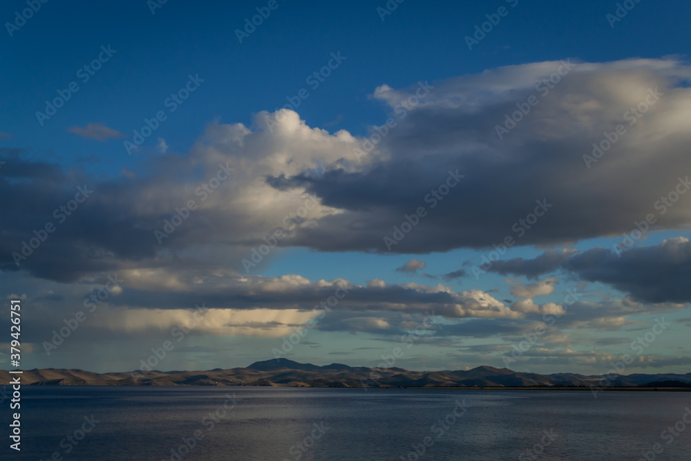 view of the clear calm undulating blue water of Lake Baikal, evening mountains on the horizon, sunset clouds background