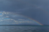 view of the clear calm undulating blue water of Lake Baikal, mountains on the horizon, colorful rainbow in sky