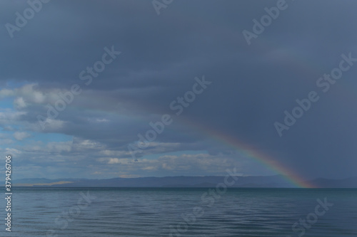 view of the clear calm undulating blue water of Lake Baikal  mountains on the horizon  colorful rainbow in sky