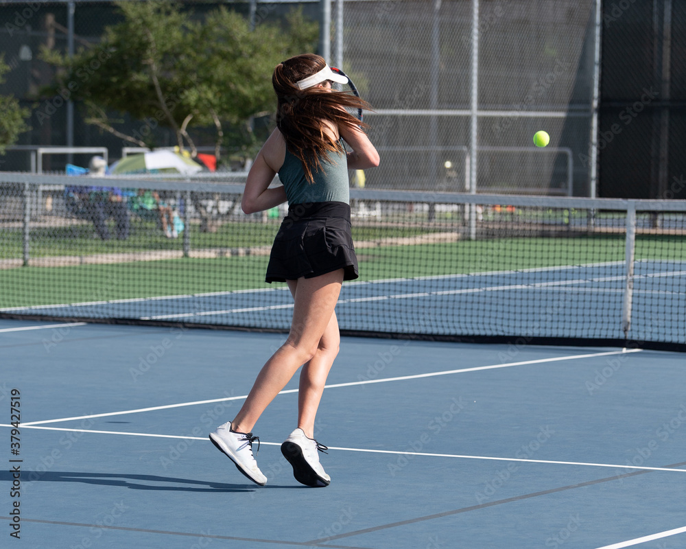 Girl playing tennis and hitting the ball over the net during a volley Girl playing tennis and hitting the ball over the net during a volley