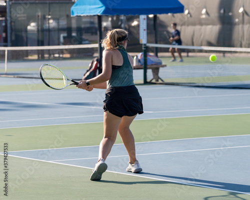 Girl playing tennis and hitting the ball over the net during a volley © Joe