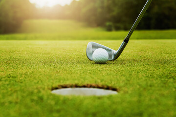 close up golf club and golf ball on green grass with sunrise background