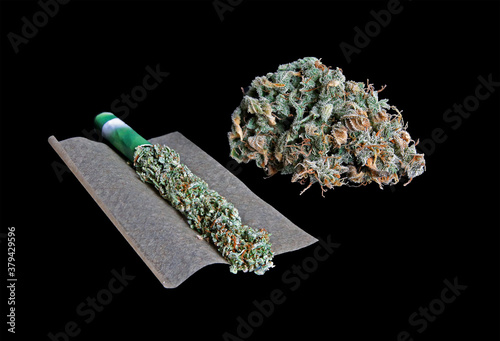 Joint of marihuana flower opened up. Paper filled with weed, grinder and pot isolated in black background. Rolling a joint and smoking cannabis. 