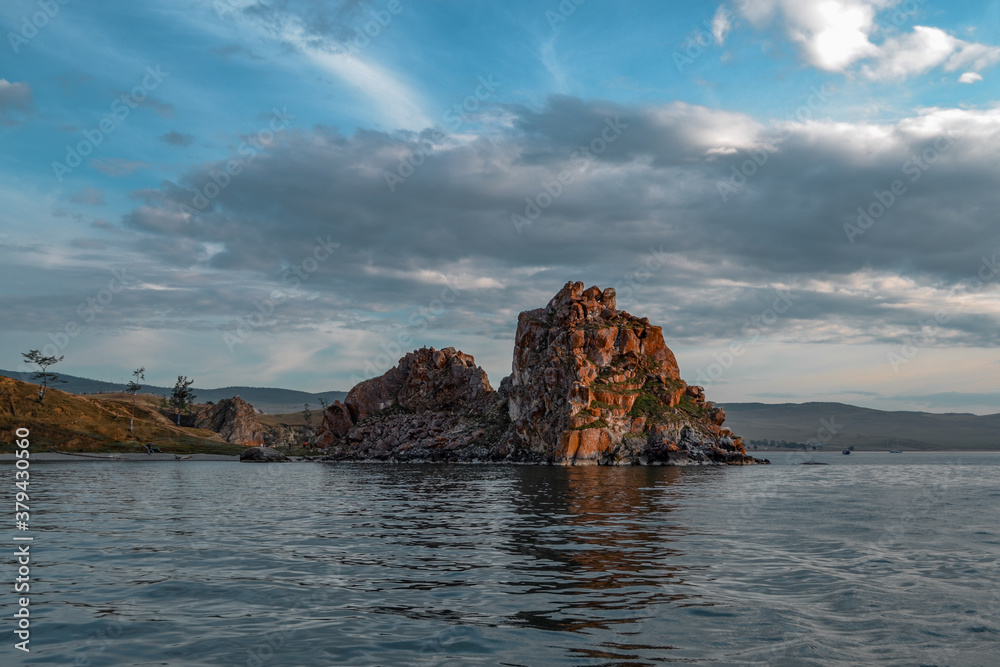 Red cape Shamanka rock in Lake Baikal, background clouds, sunset, reflection, ripples, blue sky
