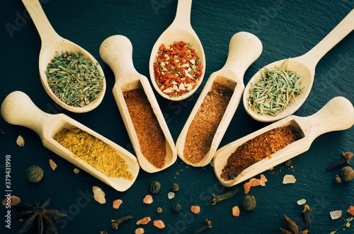 Various spices and herbsin in a wooden spoons on dark stone table. Indian cuisine. Top view. photo