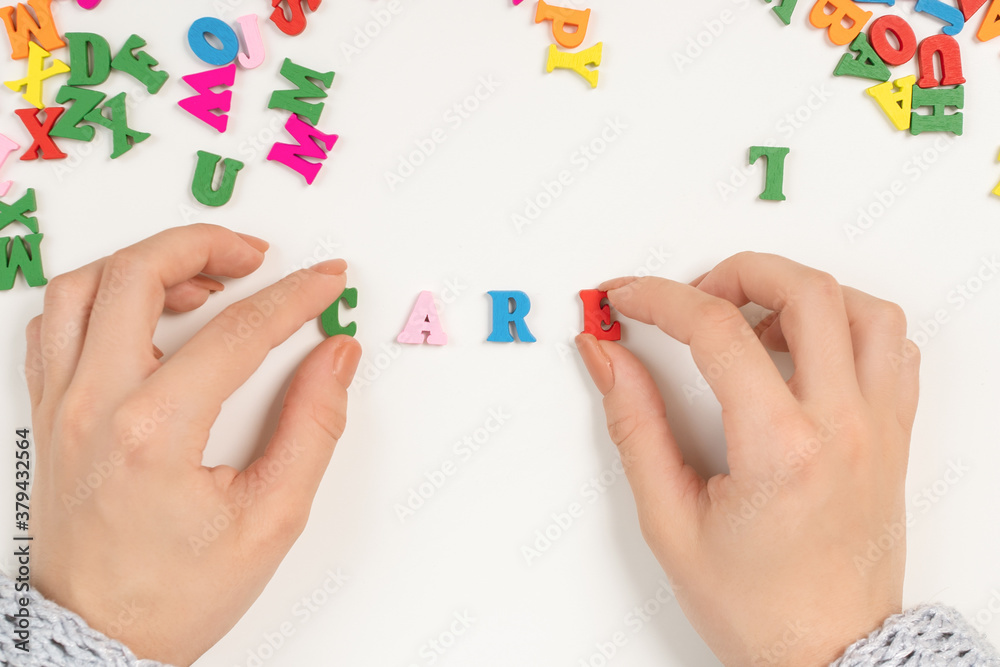 Female hands lay out the word care from colored letters Female hands lay out the word care from colored letters