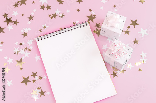 blank white notepad sheet on festive new year pink beauty background with shiny gold and white stars, beautifully wrapped gifts with bows copy space, top view, mockup © Tatyana