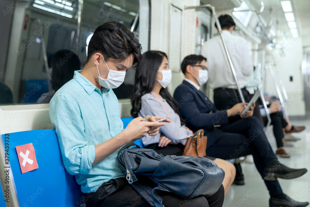 Business people using mobile phone and keep social distancing in subway. Employee wear medical hygiene face mask to prevent the outbreak of coronavirus covid-19 in sky train. New normal life concept.