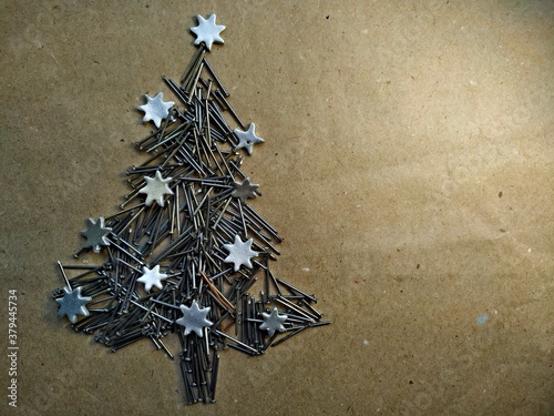 christmas tree folded from construction nails decorated silver stars on kraft paper background.