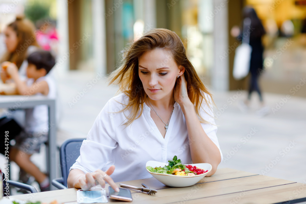 Young beautiful woman eating fresh salad in outdoor restaurant. Woman enjoying lunch bowl with fresh vegetables. Healthy food. On summer day.