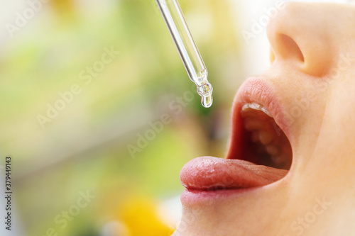 woman taking vitamin d drops in mouth from dropper. copy space photo